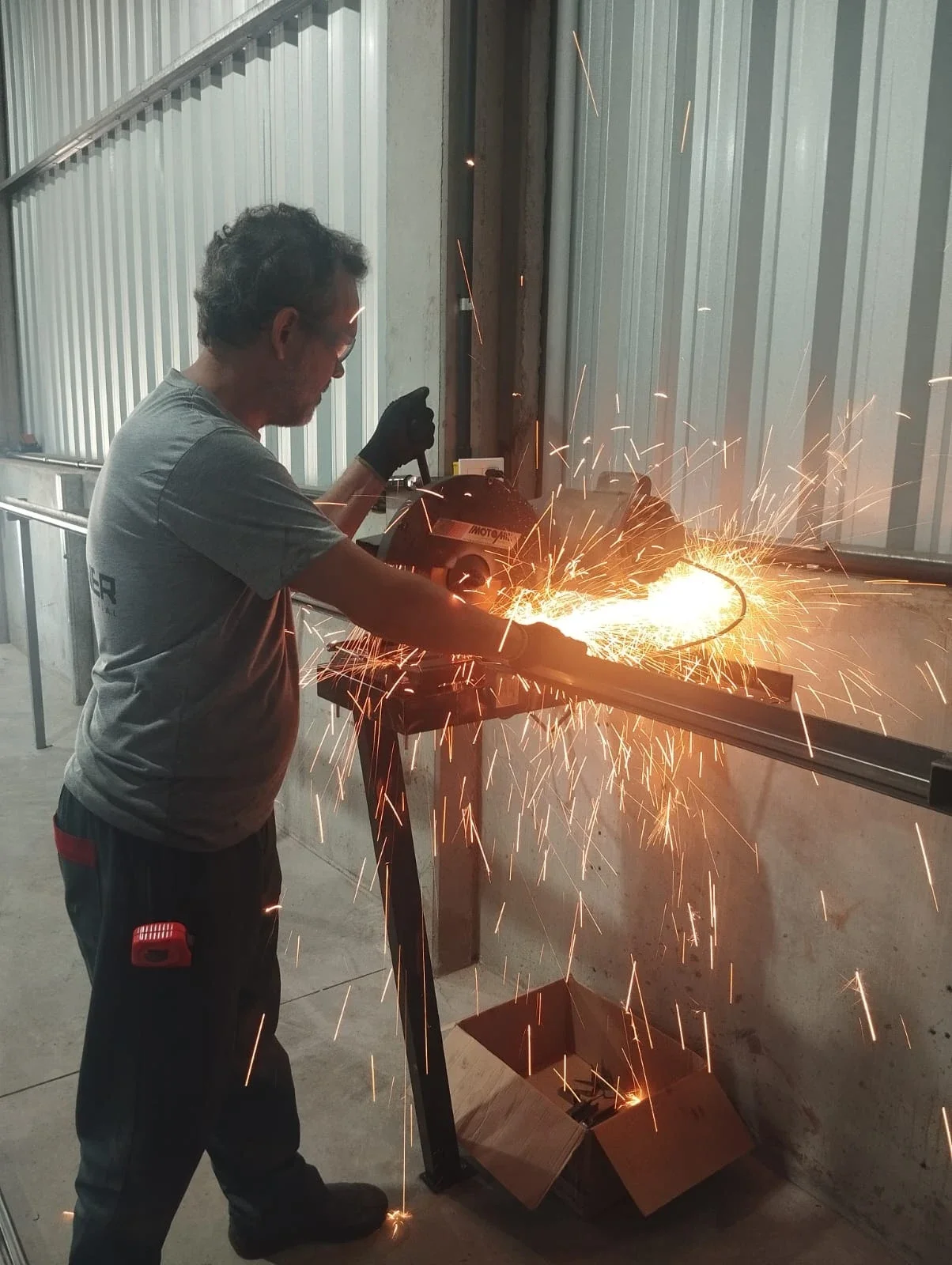 Profissional da Schreiner cortando perfil metálico na oficina, com faíscas — fabricação de estruturas sob medida