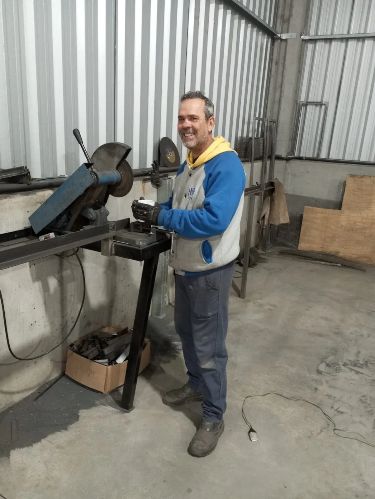 Profissional da Schreiner sorrindo na oficina, ao lado da serra de corte de metal — execução artesanal sob medida